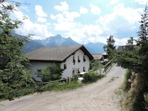 A rural road leading to a white building with a sloped roof, surrounded by greenery and mountains in the background. - Tschlin Chasa La Resgia, (Tschlin) by Interhome (Tschlin)