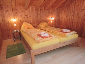 Een houten kamer met twee bedden, een kleine tafel en twee wandlampen.