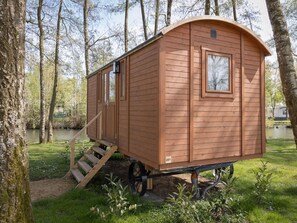 Eine Holzhütte mit einer Rampe zum Eingang, gelegen in einem bewaldeten Gebiet mit einem Teich im Hintergrund.