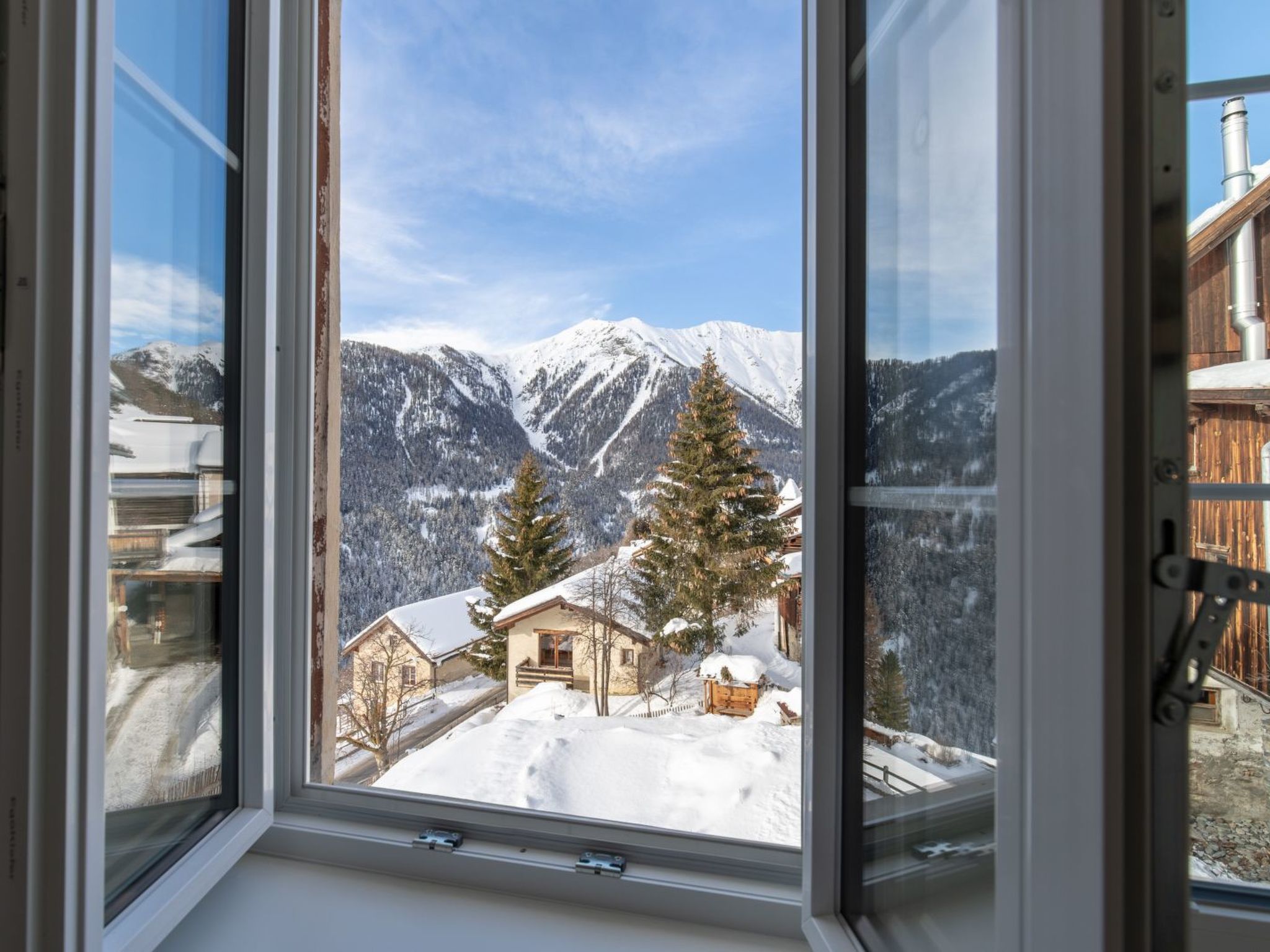 A window with a view of a snow-covered mountain landscape, a wooden cabin, and a clear sky.