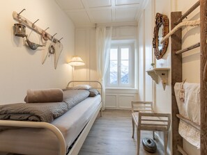 A bedroom with a bed, a bedside table, a chair, a window with curtains, and wall-mounted decorations. - Zollhaus, (Vnà) by Interhome (Vnà)
