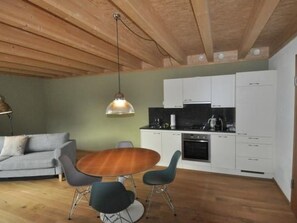 Ein gemütlicher Wohnbereich mit Holzboden, einer Küchenzeile, einem Essbereich mit rundem Tisch und Stühlen sowie einem Sofa.