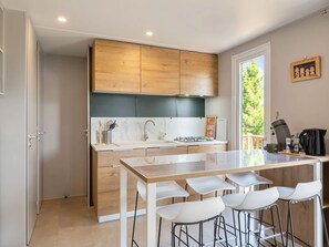 Une cuisine moderne avec des meubles en bois, un îlot central doté de tabourets, une cuisinière encastrée et une fenêtre donnant sur un espace verdoyant.