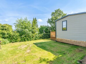 Une maison mobile avec un jardin clôturé, une pelouse verdoyante et des arbres en arrière-plan.