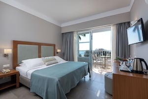 Habitación de hotel con cama, mesita de noche con teléfono, escritorio con cafetera y balcón con mesa y sillas.