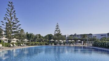 A swimming pool with lounge chairs and umbrellas, surrounded by trees and hotel buildings.