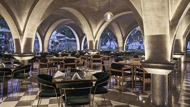 A spacious dining area with high ceilings and arched columns, featuring tables and chairs arranged for dining. - Atlantica Beach Resort (Kos)