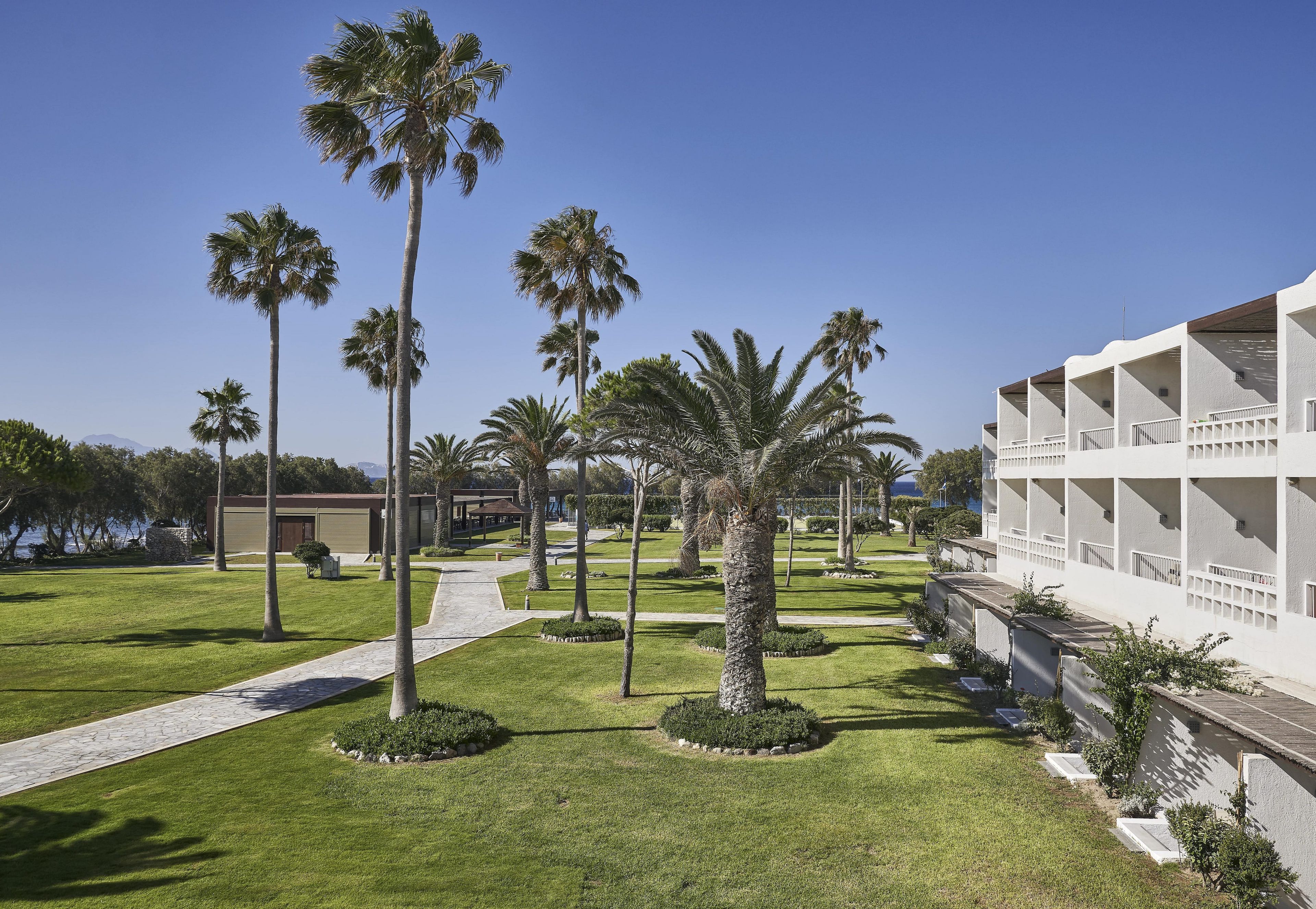 A hotel with a modern design, featuring a central pathway, palm trees, and a pool area.