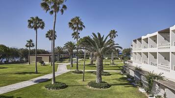 A hotel with a modern design, featuring a central pathway, palm trees, and a pool area.
