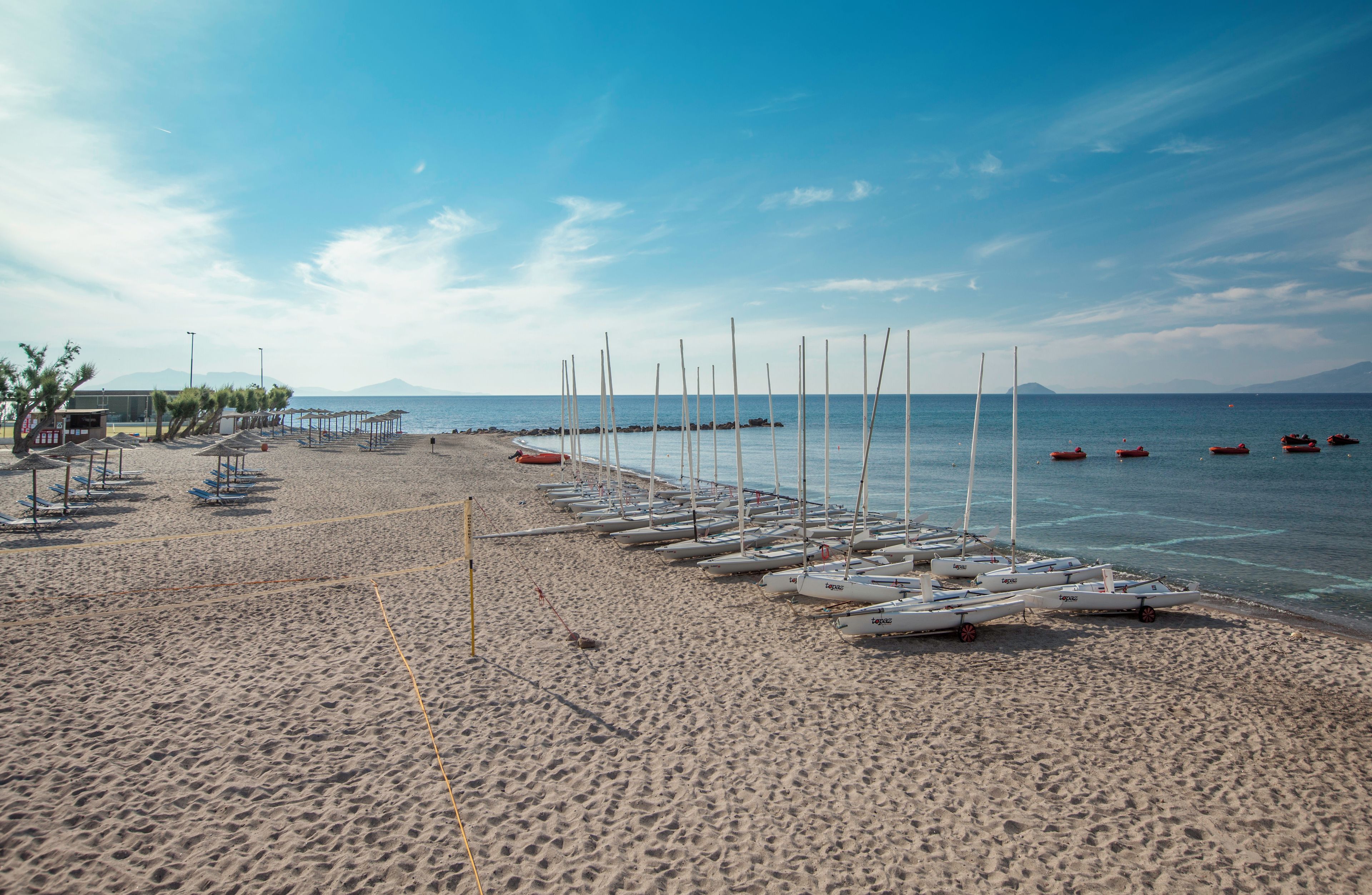 A beach with rows of sailboats, a lifeguard tower, and a clear sky.
