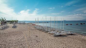 A beach with rows of sailboats, a lifeguard tower, and a clear sky.