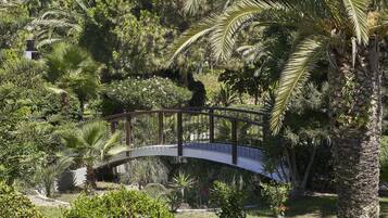 Een gebogen brug over een tuin met verschillende planten en een palmboom.