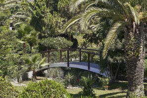 A curved bridge over a garden with various plants and a palm tree. - Atlantica Beach Resort (Kos)