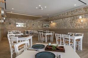 Un restaurante con mesas y sillas blancas, paredes de piedra e iluminación colgante.