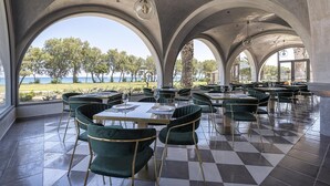 A restaurant with a checkered floor, green velvet chairs, and large arched windows overlooking a scenic view. - Atlantica Beach Resort (Kos)