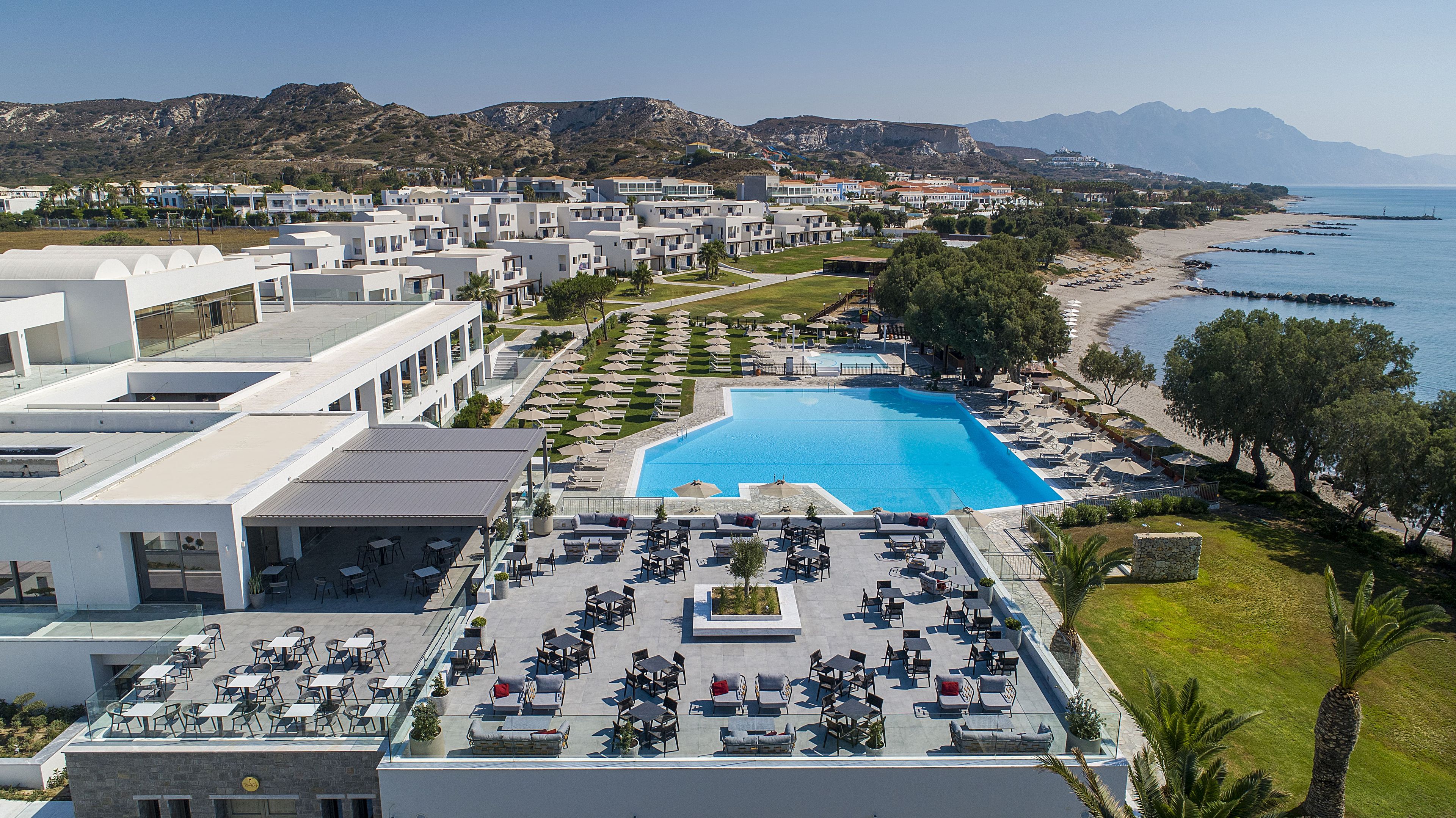 A resort with a swimming pool, outdoor seating, and a view of the beach and mountains.
