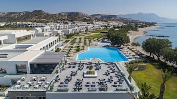 A resort with a swimming pool, outdoor seating, and a view of the beach and mountains.