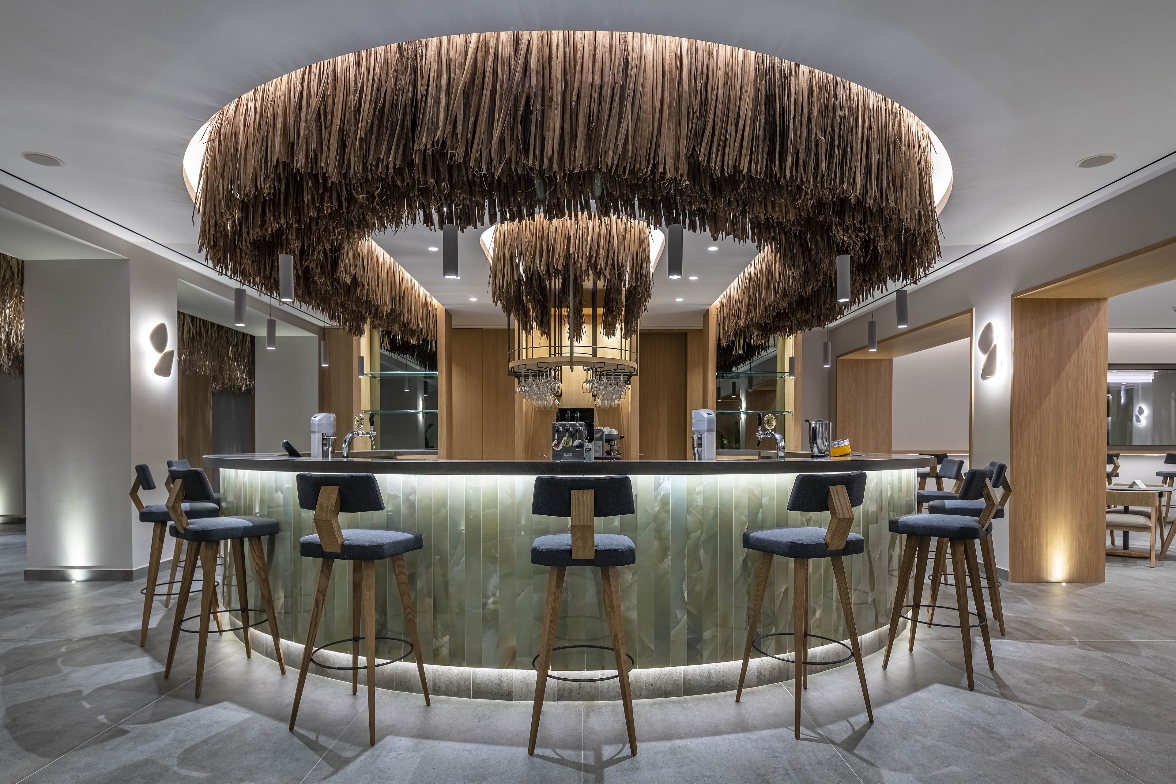 A modern bar area with a circular wooden ceiling design, bar stools, and a marble countertop.
