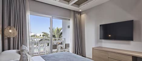 A modern bedroom with a large bed, a TV, and a balcony with outdoor furniture.