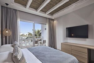 Un dormitorio moderno con una cama grande, televisión y balcón con mobiliario exterior.