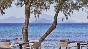 A seaside table with two glasses, a tree, and a view of the sea and mountains.