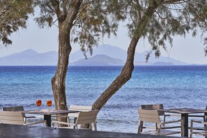 Una mesa frente al mar con dos vasos, un árbol y vistas al océano y las montañas.