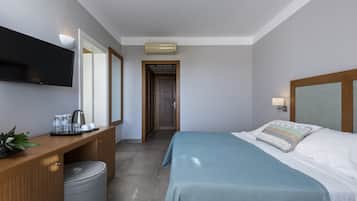 A hotel room with a bed, a desk with a flat-screen TV, a coffee maker, and a trash bin.
