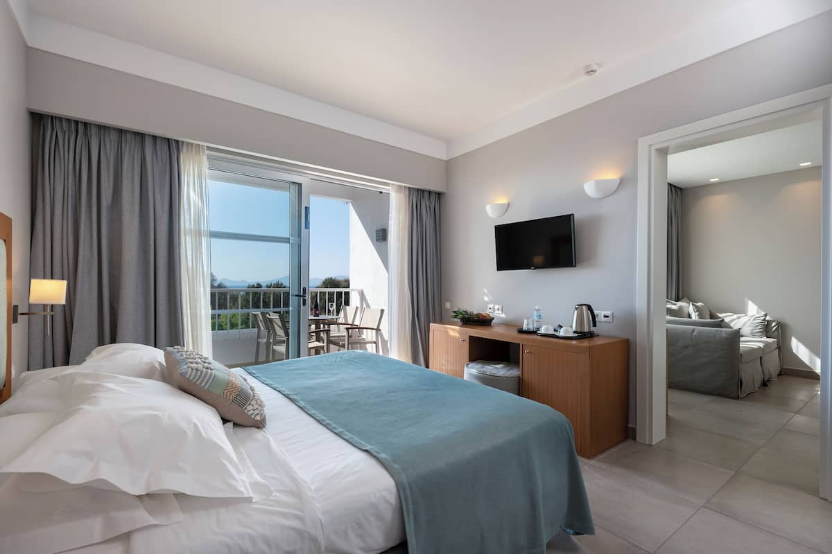 A modern hotel room with a large bed, a desk, a flat-screen TV, and a balcony with a view.