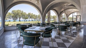 A restaurant with a checkered floor, green velvet chairs, and large arched windows overlooking a scenic view. - Atlantica Beach Resort (Kos)