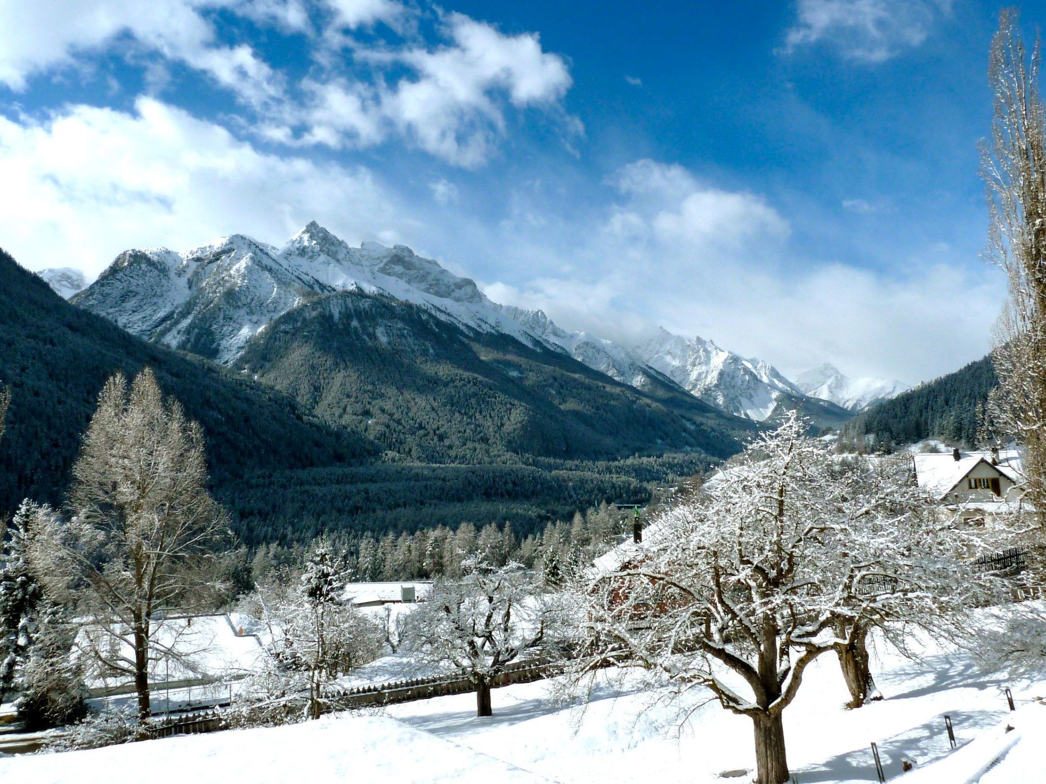 Paesaggio innevato con catena montuosa, alberi e un piccolo edificio.