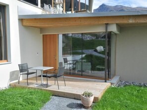 A modern house with a patio, a wooden door, and a glass sliding door leading to a garden. - Chasa Paoletta, (Ramosch) by Interhome (Ramosch)