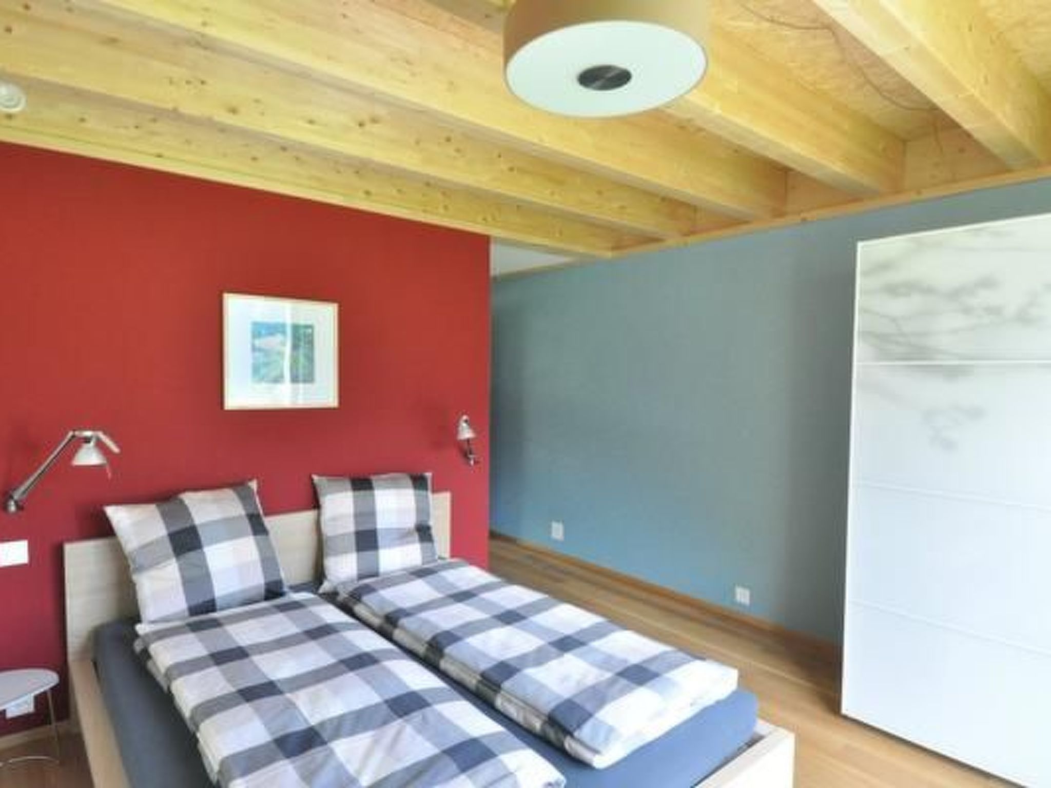 Ein Schlafzimmer mit einem Bett, einer roten Wand, einer blauen Wand und einer Holzbalkendecke.