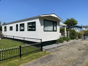 Ein eingeschossiges Haus mit flachem Dach, einem großen Fenster zur Vorderseite und einem schwarzen Zaun davor.