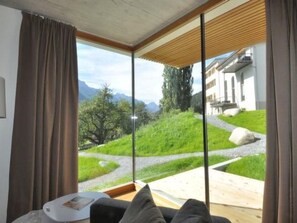 A room with a large window offering a view of a green landscape and a building. - Chasa Paoletta, (Ramosch) by Interhome (Ramosch)