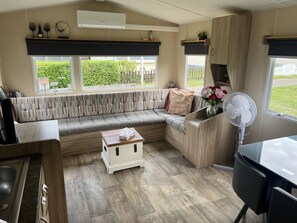 A cozy RV interior with a sectional sofa, a small table, a fan, and a kitchen area. - RBR 166 - Beach Resort Kamperland by Interhome (Kamperland)