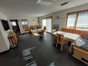 Ein modernes Wohnzimmer mit einer Couch, einem Sessel, einem Esstisch und einem Fernseher.
