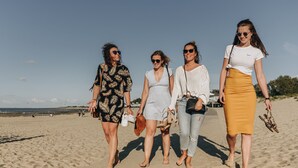 Quatre persones caminen sobre una platja sorrenca sota un cel serè.