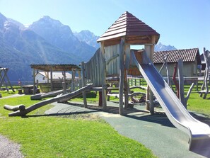 Un terrain de jeux avec un toboggan et des structures d’escalade, le tout situé dans un cadre magnifique, avec des montagnes en toile de fond.