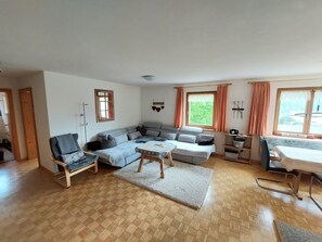 A spacious living room with a sofa set, a coffee table, a chair, and a dining table. - Ferienhof PUA - Erlebnisferien auf dem Bauernhof, (Sent) by Interhome (Sent)