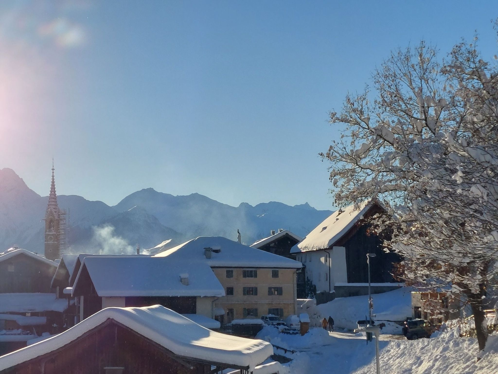 A snow-covered village with traditional buildings, a church spire, and mountains in the background.