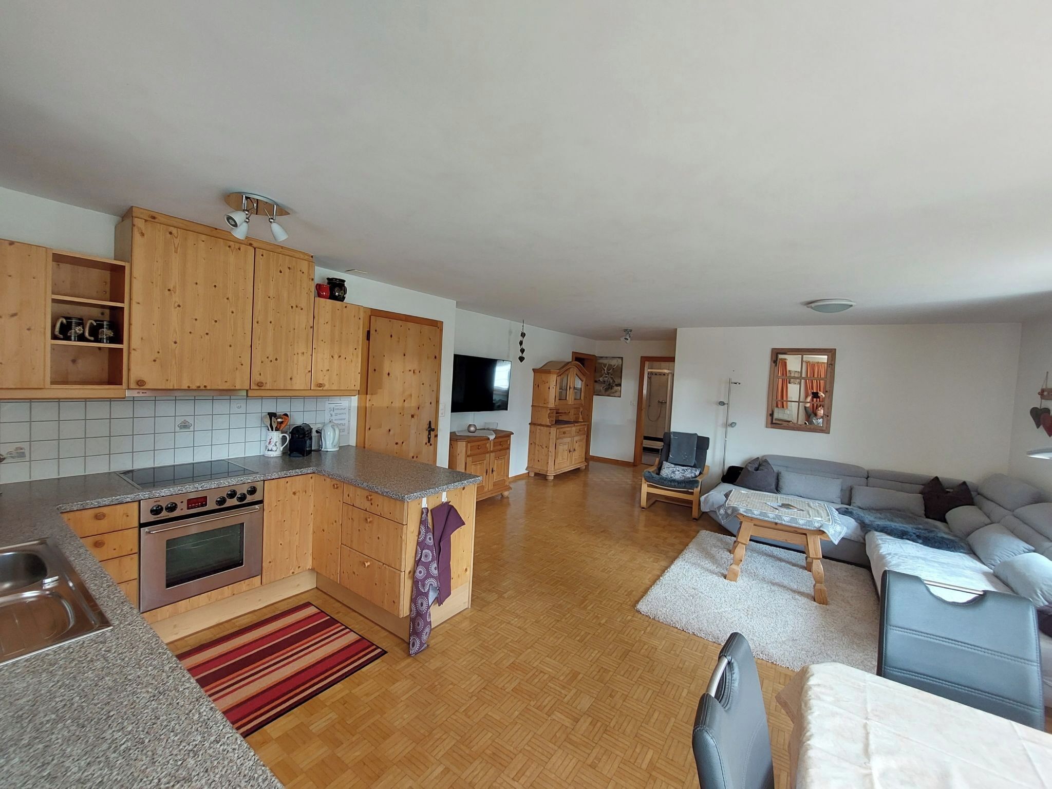Uma sala de estar ampla, com cozinha, armários de madeira, um sofá e uma televisão.