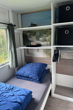 Een kamer met een bed, een plankje met een stranddecoratie, en een raam met gordijnen.