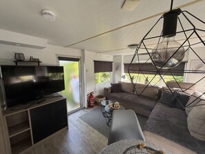A modern living room with a flat-screen TV, a sofa, a coffee table, and a hanging light fixture. - RBR 168 - Beach Resort Kamperland by Interhome (Kamperland)