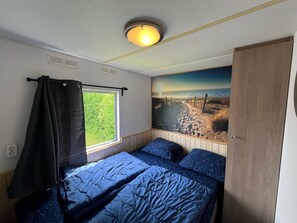 A bedroom with a bed, a window with a curtain, a wall with a beach mural, and a ceiling light. - RBR 168 - Beach Resort Kamperland by Interhome (Kamperland)