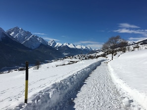 A snow-covered mountain path with a clear sky and distant snow-capped peaks.