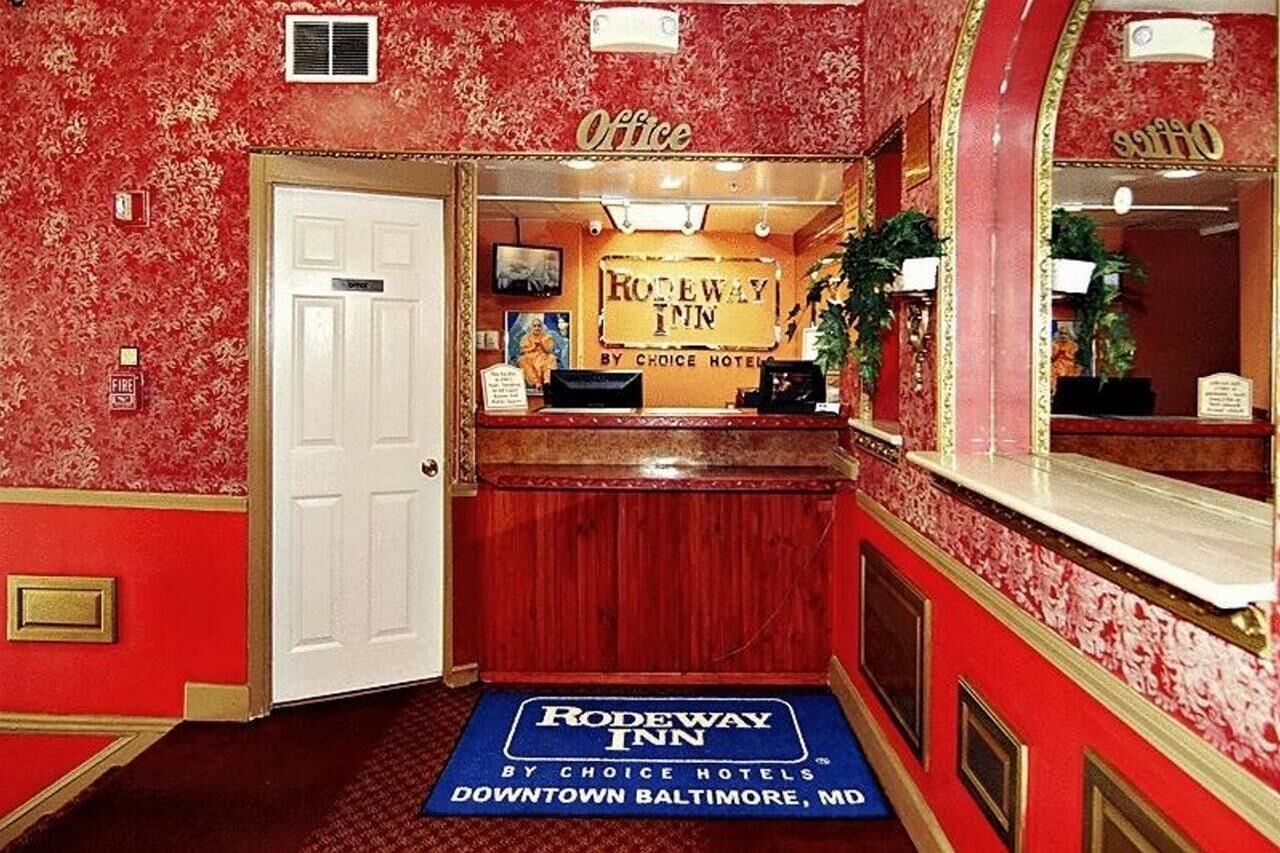 Una zona de recepción con papel tapiz floral rojo, una puerta blanca y un cartel del Rodeway Inn by Choice Hotels en el centro de Baltimore, MD.