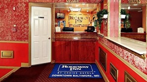 A reception area with a red floral wallpaper, a white door, and a sign for the Rodeway Inn by Choice Hotels in Downtown Baltimore, MD. - Midtown inn (Baltimore)