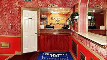 Una zona de recepción con papel tapiz floral rojo, una puerta blanca y un cartel del Rodeway Inn by Choice Hotels en el centro de Baltimore, MD.