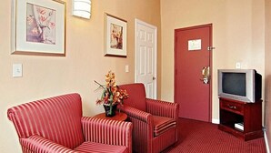 A room with striped red chairs, a small table with flowers, a television on a wooden stand, and a red door. - Midtown inn (Baltimore)