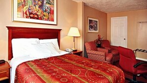 A hotel room with a bed, a desk, a chair, a lamp, and two paintings on the wall. - Midtown inn (Baltimore)